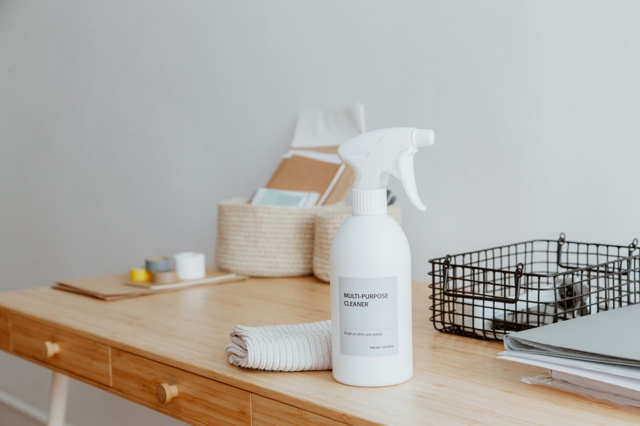 about-us-01 Minimalist desk with a focus on a multipurpose cleaner, office supplies, and storage solutions.