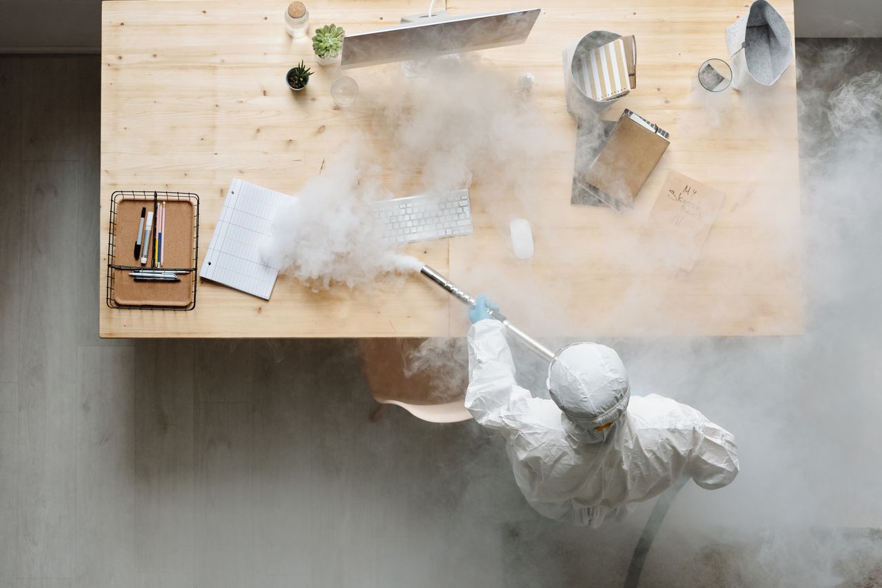 about-us-02 An individual disinfects a workspace using fumigation, wearing full protective gear for safety.